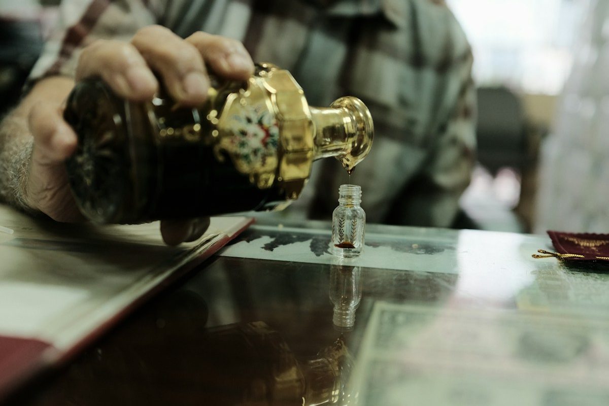 Oud oil being poured from an ornate gold bottle into a small vial